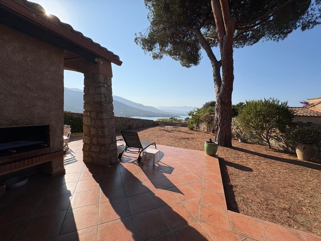 Terrasse de la villa de Sagone avec barbecue en pierre, pin parasol et vue sur le golfe